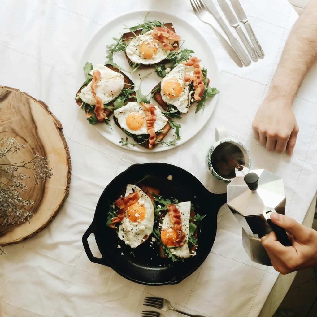 From above of crop unrecognizable person pouring coffee in mug while sitting at table with fresh toasts with eggs and ham